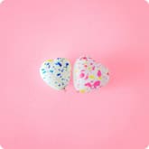 Two decorated heart-shaped cookies with colorful sprinkles on a pink background.